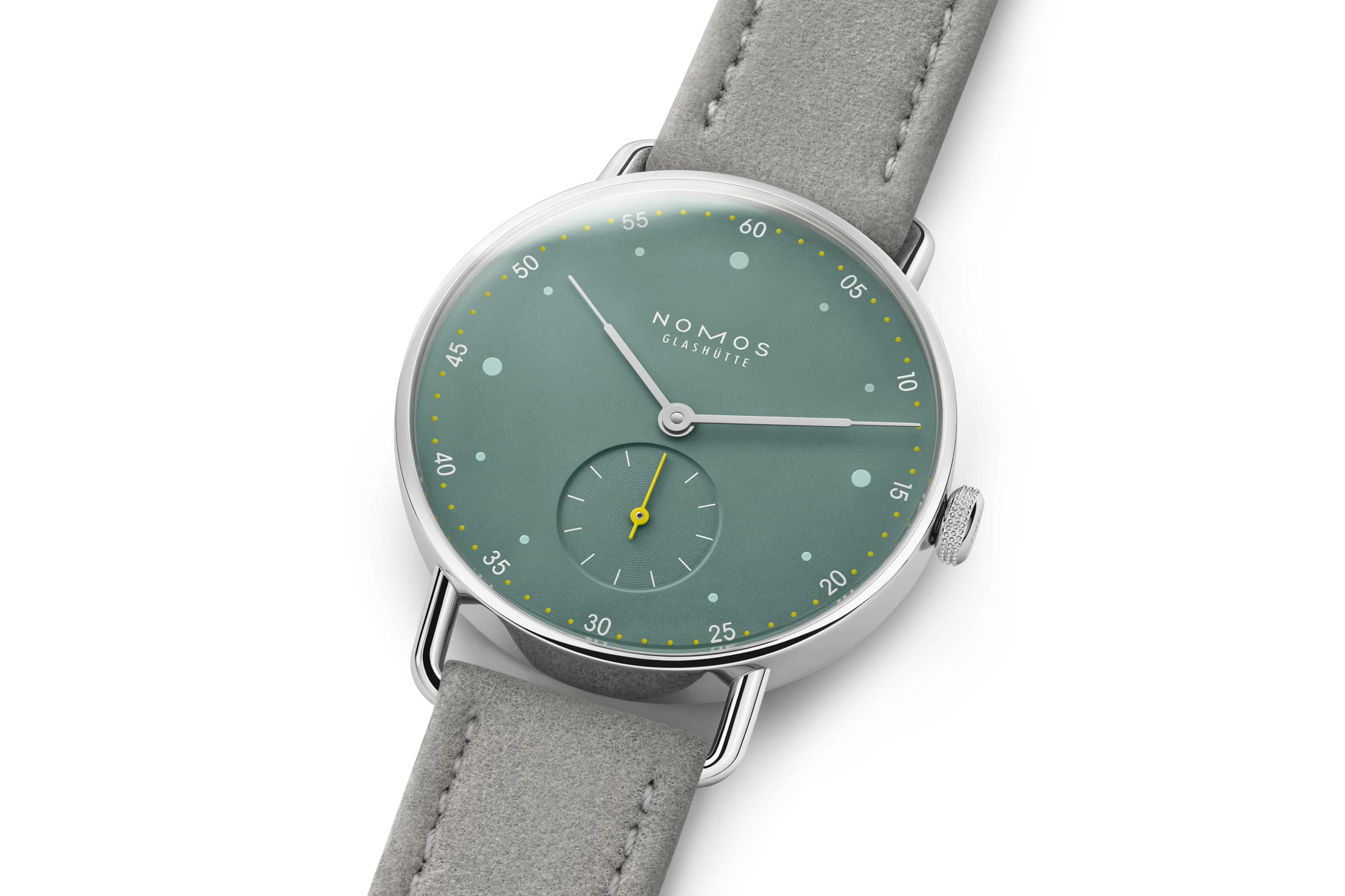 NOMOS Glashütte / METRO 33 / NM1124スタイリッシュなメトロの10周年に向けて、フェミニンなサイズ33のSSケースがファミリーに加わります。  大都会をイメージしたメトロ33は輝くガラス張りのビル（オールシルバー）・ブルックリンによくみられる赤煉瓦の建物（ミュートレッド）・公園や自由の女神の心豊かな緑（セージ）の3色です。  複雑なダブルカーブのサファイアクリスタルガラス、繊細なワイヤーラグ、また時計師が使う道具をモチーフにした特徴的なメトロリューズなど、すべてが非の打ちどころのないグラスヒュッテのクラフツマンシップと最高基準のデザインです。  時計のデザインを引き締めているのはライトグレーのヴィーガンベロアストラップ。スマートで遊び心があり、エネルギーに満ちている現代的なエレガンスを表現している3種類のメトロは、女性でだけでなくもちろんスレンダーな腕周りの男性にも似合います。