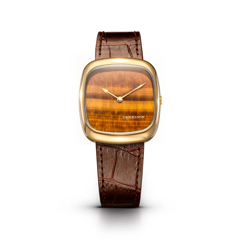 ALD Collection　Natural Stone Tiger Eye In Gold　ALD-G-ST03-BRN-R-GBKL　ダイヤルには天然タイガーズアイ（虎目石）を採用。温かみのあるブラウンゴールドの色調と、奥行きのある独特な模様が特徴で、一本ごとに異なる表情を楽しめます。丁寧にカット・ポリッシュされた天然石が、控えめながらも確かな存在感を放ちます。 ケースはゴールドPVD仕上げのステンレススチール製。37mm × 33.5mm、厚さ約6.05mmのスリムなプロポーションが、ドレスウォッチとしての品格と日常使いの快適さを両立。型押しのブラウンレザーストラップと、ケースの曲線美に呼応する特別仕様のピンバックルが、全体の統一感を高めています。